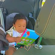 Kyzeir Walker is registered to the contest to win money with this photo: toddler, child, car_seat, book, vehicle_interior, seat, window, seatbelt, child_safety, toy, infant, car, reading, baby, casual, portrait, seat_headrest, clothing, seat_belt, heart_doodle