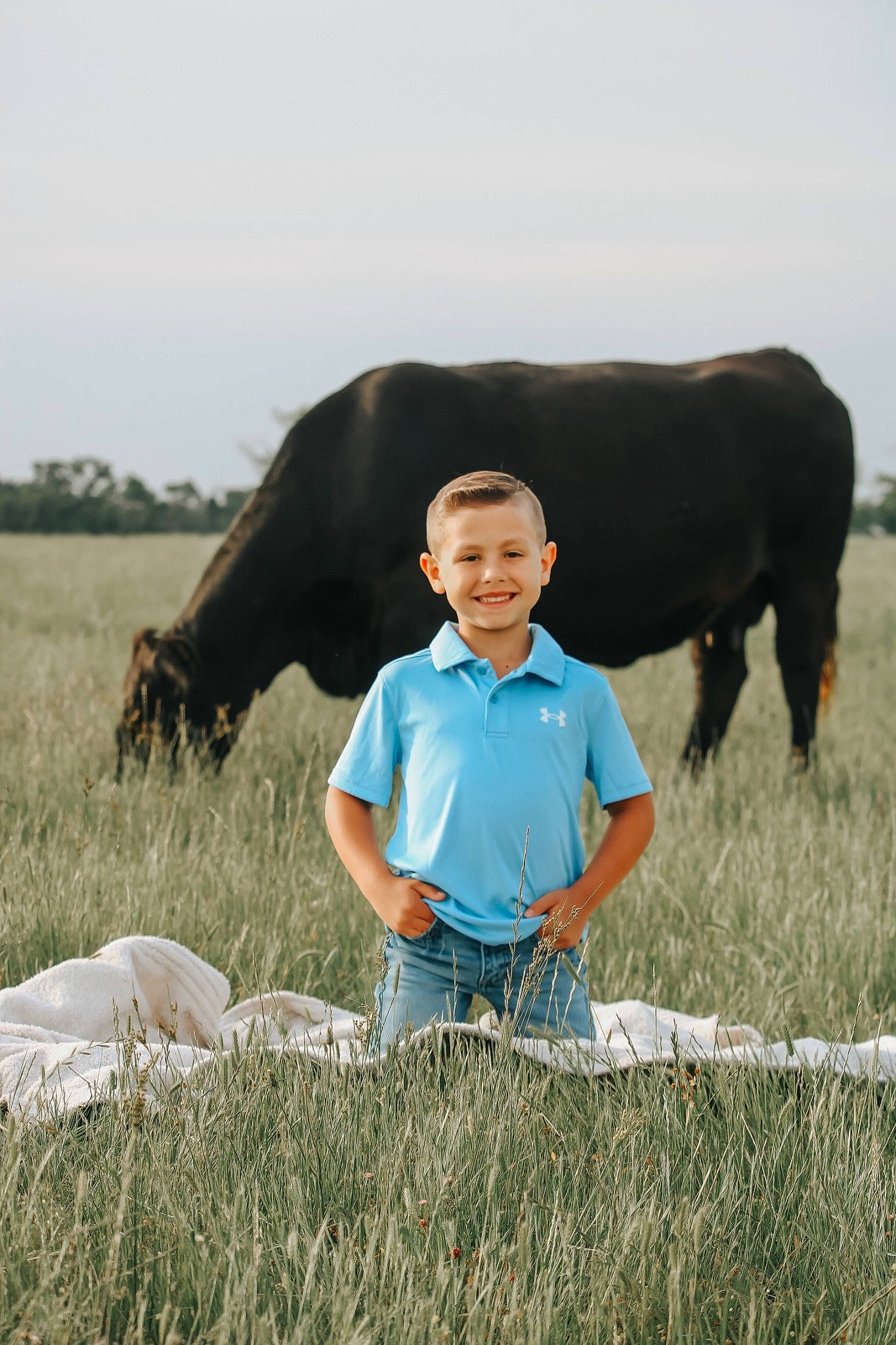 Liam is registered to the contest to win money with this photo: agriculture, dairy_cow, grass, grassland, grazing, happy, joy, landscape, livestock, meadow, people_in_nature, person, plain, plant, prairie, rural_area, sky, smile, summer, t_shirt