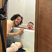 Letty joined the competition — help win amazing prizes! man, baby, bathtub, bathroom, smile, happy, tattoo, curly_hair, floor, door, towel, water, skin, person, indoor, interaction, joy, family, playful, candid