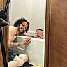 man, baby, bathtub, bathroom, smile, happy, tattoo, curly_hair, floor, door, towel, water, skin, person, indoor, interaction, joy, family, playful, candid