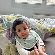 Salman participe au concours pour gagner de l'argent avec cette photo : baby, child, infant, bed, blanket, window, hand, finger, person, indoor, clothing, bib, curly_hair, face, cute, smiling, sitting, cozy, home, natural_light