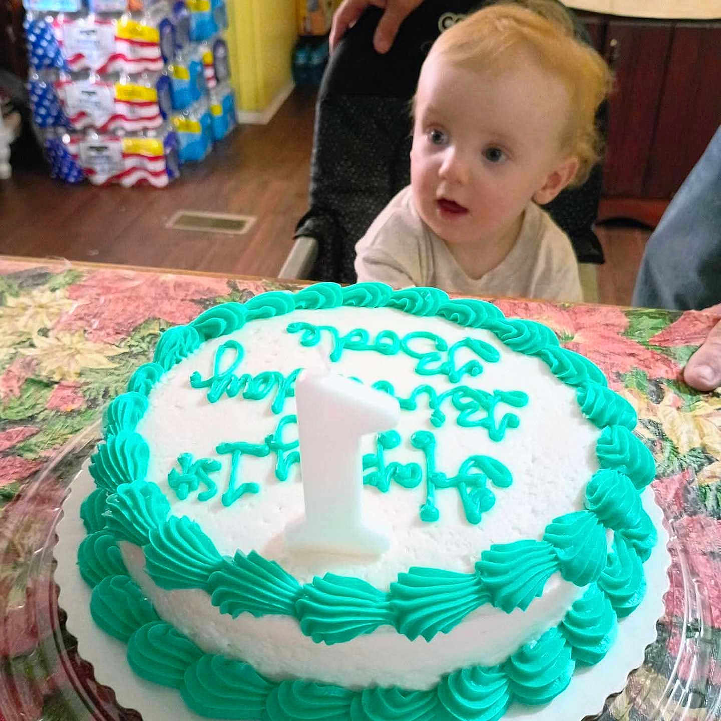 Bode Reed Jolly is registered to the contest to win money with this photo: baby, cake, birthday_cake, candle, high_chair, kitchen, child, icing, number_candle, table, curious, celebration, person, food, indoor, hand, frosting, plastic_container, decorated_cake, young_child