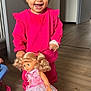 toddler, child, smiling, pink_clothing, doll, toy, indoor, wooden_floor, happy, person, curly_hair, playtime, cute, young_child, portrait, standing, home, flooring, bright, casual