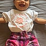 baby, child, smiling, happy, infant, clothing, shirt, shorts, plaid, pink, purple, lying_down, bed_sheet, cute, face, teeth, arms_outstretched, casual, indoors, portrait