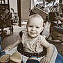 Rylee is registered to the contest to win money with this photo: baby, walker, child, tongue_out, smile, porch, clutter, door, chair, toy, outdoor, tree, box, seat, person, furniture, floor, hand, expression, sepia