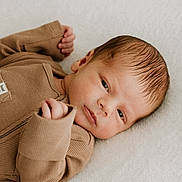 Hugo is registered to the contest to win money with this photo: newborn, baby, infant, face, clothing, brown, ribbed, hands, lying_down, blanket, soft_texture, peaceful, portrait, closeup, skin, head, expression, cute, child, indoors
