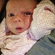 Sophia joined the competition — help win amazing prizes! baby, newborn, infant, face, eyes, mouth, pink_clothing, patterned_onesie, swaddle, arm, parent_arm, closeup, portrait, indoor, bed, blanket, skin, cozy, sleepy, cradle