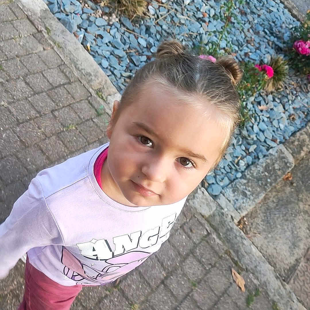 Lyana participe au concours pour gagner de l'argent avec cette photo : blue_stones, casual_clothing, child, cobblestone_path, curious_expression, cute, daylight, garden_bed, greenery, happy, nature, outdoor, person, pink_flowers, portrait, sidewalk, tree_trunk, twin_buns, white_shoes, young_girl