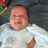 Kaige is registered to the contest to win money with this photo: baby, infant, smiling, onesie, sheep, blanket, toy, floor, child, cute, sleepy, clothing, lying_down, indoors, person, soft, cozy, toddler, happy, face
