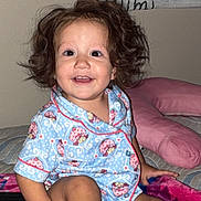 Clairann is registered to the contest to win money with this photo: bed, blanket, blue_clothing, child, cozy, curly_hair, cute, face, happy, home, indoor, pajamas, person, pink_blanket, playful, plush_toy, sitting, smiling, toddler, wall_art