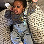 baby, infant, child, cushion, clothing, denim, sock, face, person, cute, indoor, fabric, pattern, text, comfort, relaxing, raising_hand, smiling, black_hair, casual