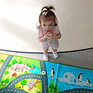Willow Mae is registered to the contest to win money with this photo: toddler, child, indoor, play_mat, colorful, toy, clothing, socks, animal_illustrations, panda, penguin, dolphin, koalas, rhino, road_pattern, person, looking_up, hair_bow, curious, floor