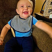 Carbon is registered to the contest to win money with this photo: baby, child, smiling, blue_clothing, striped_bib, sitting, arm_outstretched, brown_chair, indoor, happy, face, person, cute, young_child, home_interior, wooden_table, decor, teeth, portrait, infant