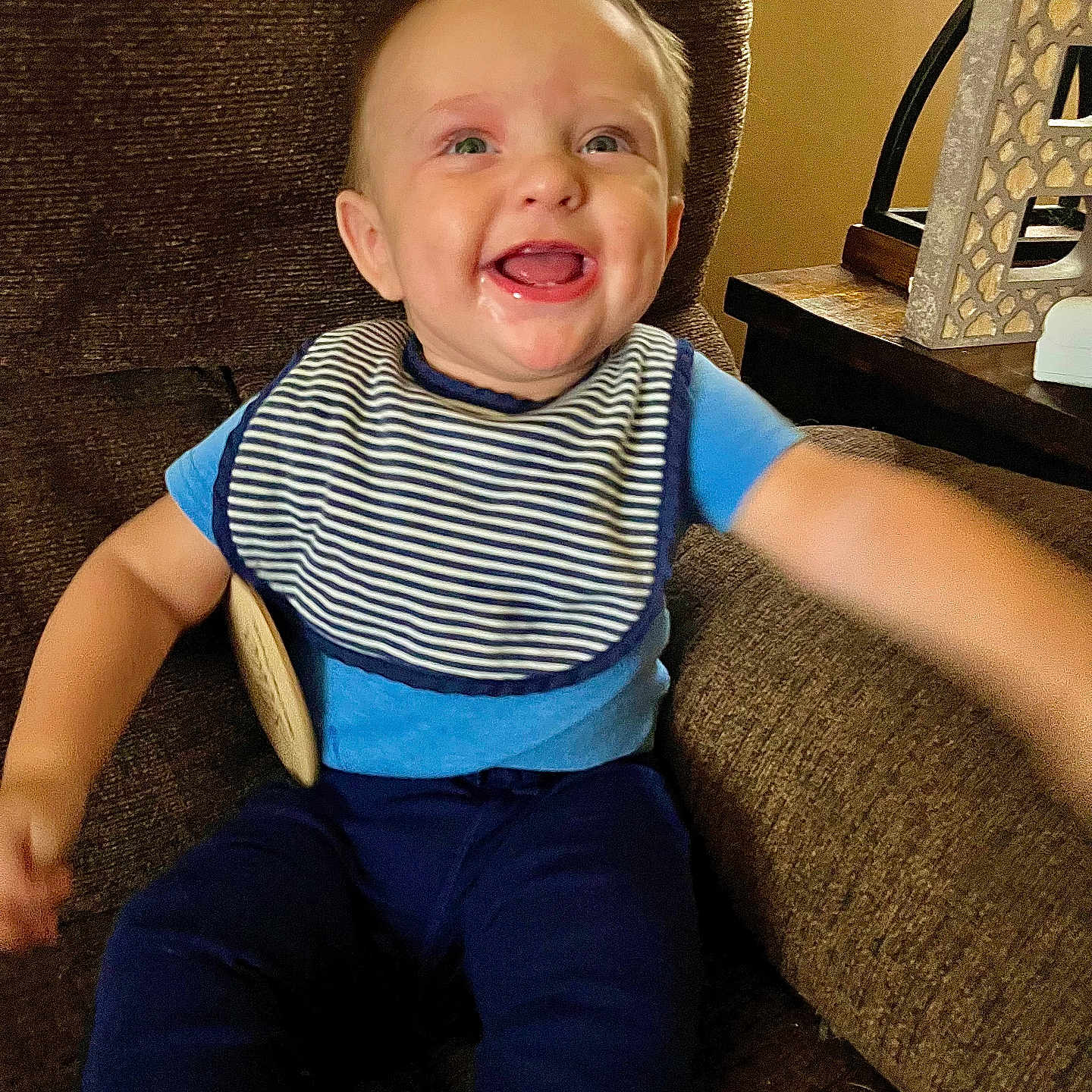 Carbon is registered to the contest to win money with this photo: arm_outstretched, baby, blue_clothing, brown_chair, child, cute, decor, face, happy, home_interior, indoor, infant, person, portrait, sitting, smiling, striped_bib, teeth, wooden_table, young_child