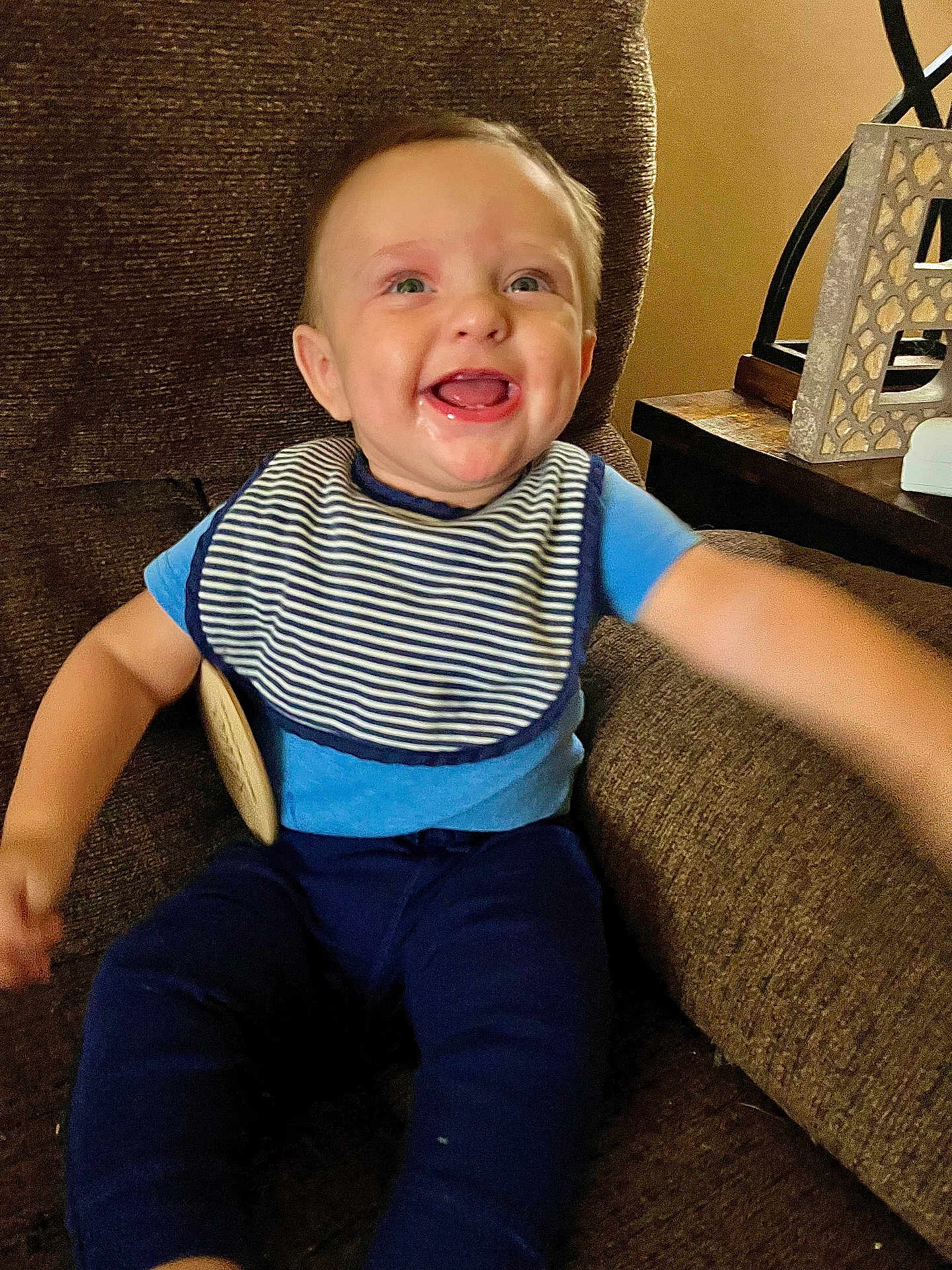 Carbon is registered to the contest to win money with this photo: baby, child, smiling, blue_clothing, striped_bib, sitting, arm_outstretched, brown_chair, indoor, happy, face, person, cute, young_child, home_interior, wooden_table, decor, teeth, portrait, infant