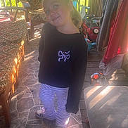 Phoebe is registered to the contest to win money with this photo: child, girl, smiling, portrait, standing, outdoor, porch, sunlight, patio, chair, clothing, toy, soccer_ball, deck, railing, garden, house, striped_pants, black_shirt, happy