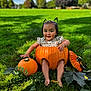toddler, child, pumpkin, grass, outdoor, autumn, smiling, greenery, leaves, nature, sunlight, blue_sky, clouds, cute, sitting, playful, holiday, fall, person, daytime