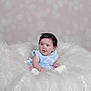 adorable, baby, blue_dress, bright, child, cozy, curious, cute, fluffy_cushion, hair_clip, happy, indoors, infant, portrait, sitting, smiling, soft_background, studio_photo, white_fur, young_child