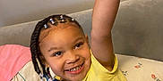 Kai'Lani Garnett joined the competition — help win amazing prizes! child, smiling, braided_hair, beads, yellow_shirt, bed, bedding, pillow, blanket, indoor, happy, person, raised_arm, cute, portrait, casual_clothing, feet, home, childhood, playful