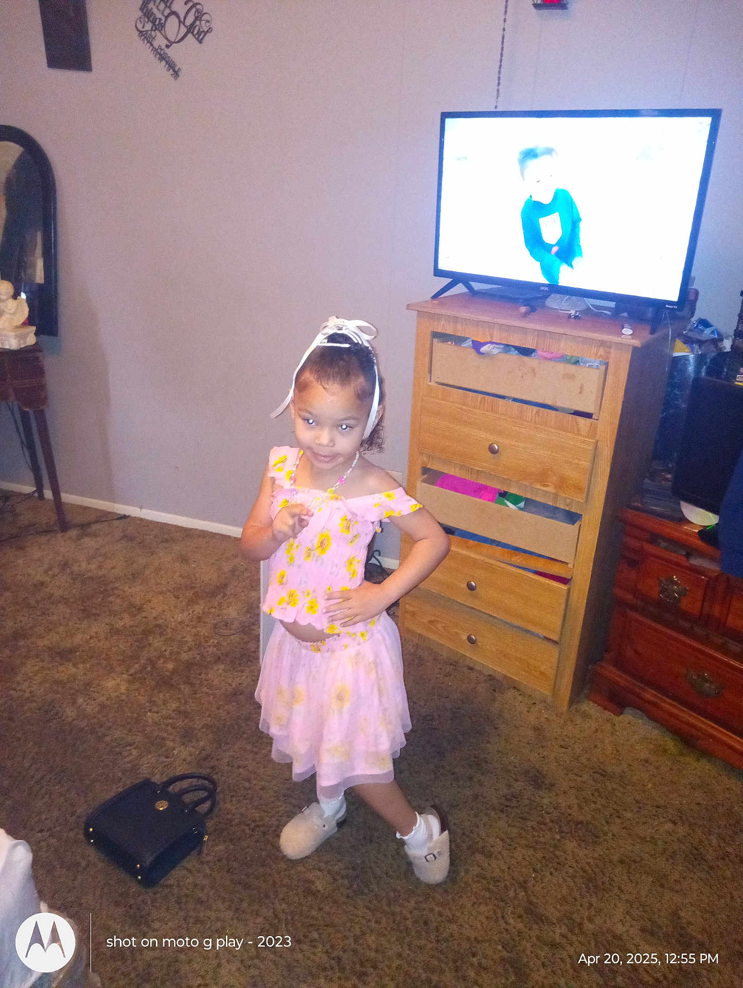Kai'Lani Garnett is registered to the contest to win money with this photo: carpet, child, decor, dresser, floor, floral_pattern, furniture, girl, hair_bow, handbag, home_interior, living_room, mirror, necklace, pink_dress, portrait, posing, slippers, smiling, television