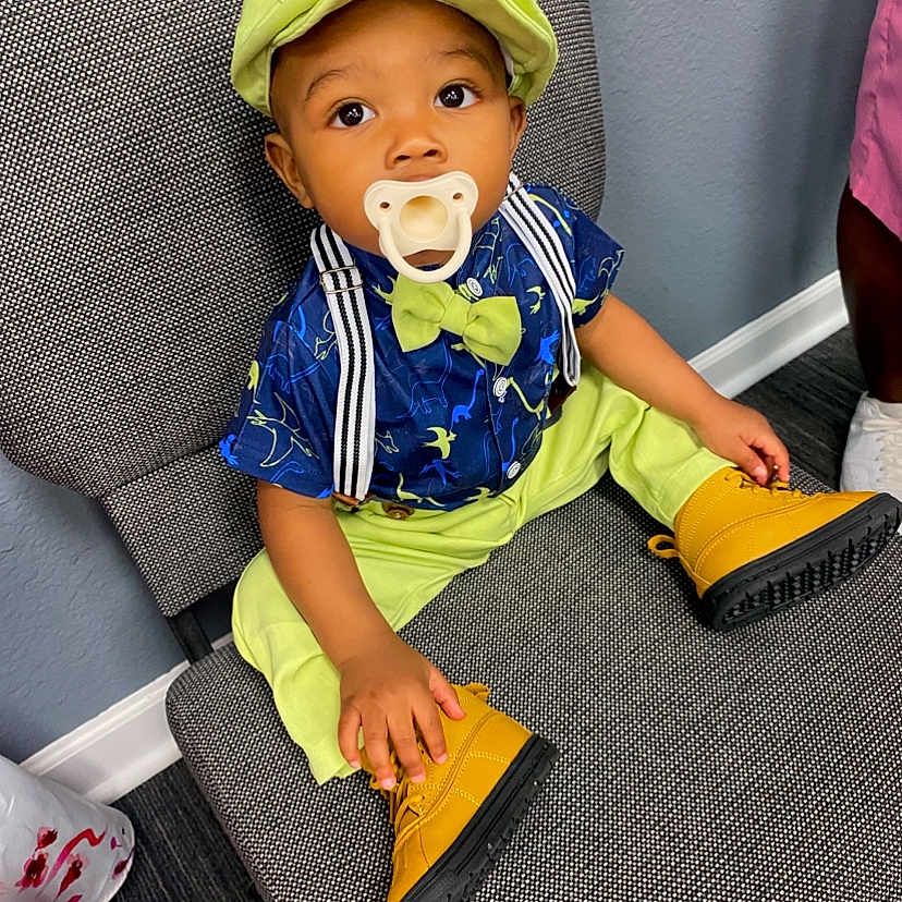 Zayven is registered to the contest to win money with this photo: baby, boots, bow_tie, chair, child, colorful, curious, cute, dinosaur_print, fashion, footwear, hat, indoor, pacifier, pants, portrait, shirt, sitting, suspenders, toddler