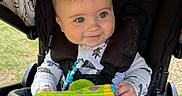 Romeo joined the competition — help win amazing prizes! baby, child, stroller, toy, smile, blue_eyes, clothing, outdoor, grass, seatbelt, cute, infant, person, happy, playful, fabric, hand, head, face, comfort