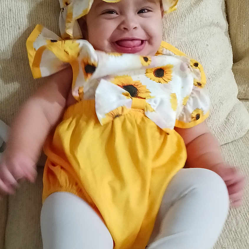 Astrid is registered to the contest to win money with this photo: baby, child, couch, cozy, cute, fabric, furniture, happy, hat, indoors, infant, person, playful, portrait, sitting, smiling, sunflower, tongue_out, white_tights, yellow_clothing