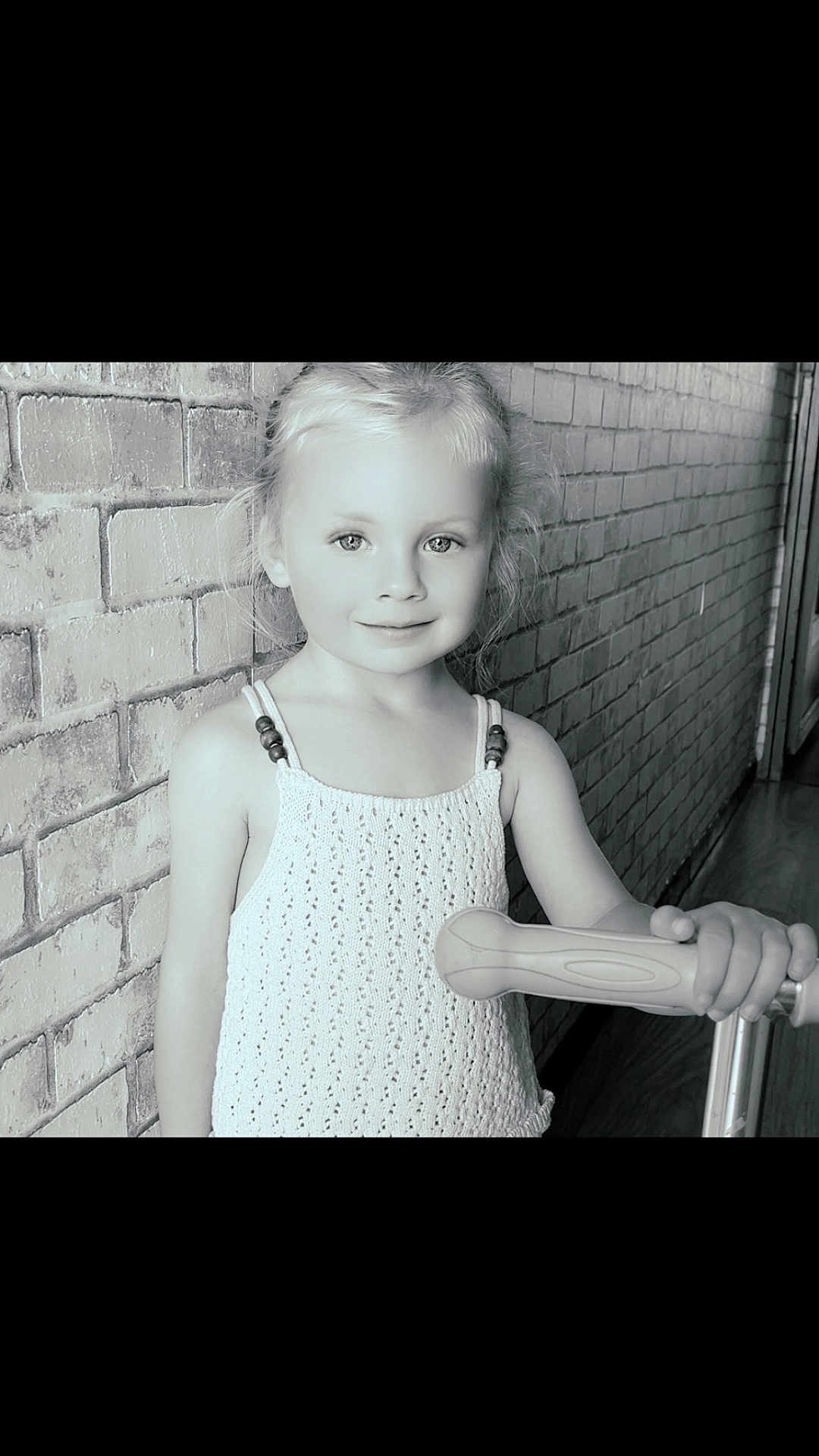 Jahnaë a rejoint le concours — aidez-le/la à gagner de superbes lots ! child, girl, scooter, brick_wall, portrait, indoor, smile, blonde_hair, knitted_top, playful, young, handle, person, cute, standing, looking_at_camera, monochrome, photography, innocence, bright_eyes