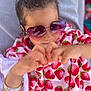 Eva is registered to the contest to win money with this photo: child, sunglasses, heart_shaped, purple, blanket, strawberry_pattern, hand_gesture, smile, hair_bun, wristband, cozy, portrait, close_up, playful, outdoor, young, person, fashion, accessory, casual