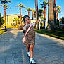 Eva is registered to the contest to win money with this photo: child, girl, smiling, posing, leopard_print, dress, white_tshirt, sneakers, pink_purse, palm_trees, sidewalk, outdoor, sunlight, shadow, blue_sky, greenery, building, happy, walking, playful