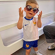 Marceau participe au concours pour gagner de l'argent avec cette photo : toddler, child, sunglasses, sport_outfit, indoor, crib, floor, tile_floor, shorts, shirt, socks, person, playful, fashion, pose, cute, home, smile, hair, footwear