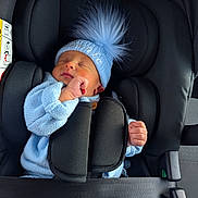 Vinnie is registered to the contest to win money with this photo: baby, newborn, car_seat, blue_hat, pom_pom, knitwear, sleeping, infant, child, safety_harness, black_car_seat, soft_light, peaceful, cute, tiny_hand, clothing, portrait, indoor, seat_belt, headwear