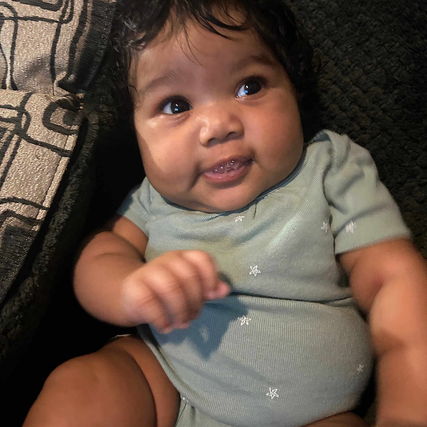 Gianni joined the competition — help win amazing prizes! baby, infant, child, onesie, smile, face, hand, curly_hair, cheeks, sitting, pillow, patterned, texture, dark_background, clothing, cute, portrait, indoors, happy, person