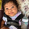 baby, infant, car_seat, bottle, milk, smile, face, hair, clothing, floral_pattern, seat_belt, child, cute, expression, indoors, person, skin, closeup, feeding, sitting