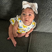 Gianni is registered to the contest to win money with this photo: baby, bow, bright_colors, child, clothing, comfortable, couch, cute, expression, face, headwear, indoors, infant, looking_up, person, sitting, skin, texture, upholstery, young