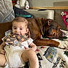 baby, blanket, brown_dog, companion, couch, cozy, dog, family, indoor, infant, lying_down, nursery, onesie, pet, portrait, sitting, sleeping, smiling, stuffed_animal, toy