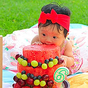 Lydia is registered to the contest to win money with this photo: baby, child, watermelon, fruit, cake, grapes, blueberries, strawberries, red_bow, headband, blanket, outdoor, grass, milestone, celebration, crawling, cute, summer, food, colorful