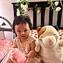 Lydia is registered to the contest to win money with this photo: baby, bottle, plush_toy, cat_plush, bed, headboard, flowers, pink, child, infant, toy, cute, indoor, person, sitting, clothing, face, hair, skin, room