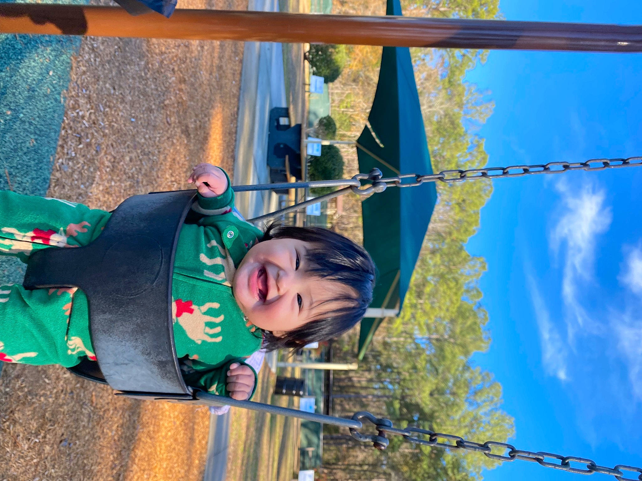 Mia is registered to the contest to win money with this photo: blue, city, cloud, electric_blue, electricity, fun, happy, joy, leisure, line, outdoor_play_equipment, person, playground, pole, public_utility, recreation, sky, smile, toddler, tree