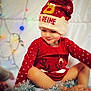 toddler, child, hat, red_clothing, christmas_hat, reindeer, tinsel, holiday_lights, smile, indoor, cute, festive, sitting, winter_clothing, pom_pom, polka_dots, background_blur, happy, portrait, cozy