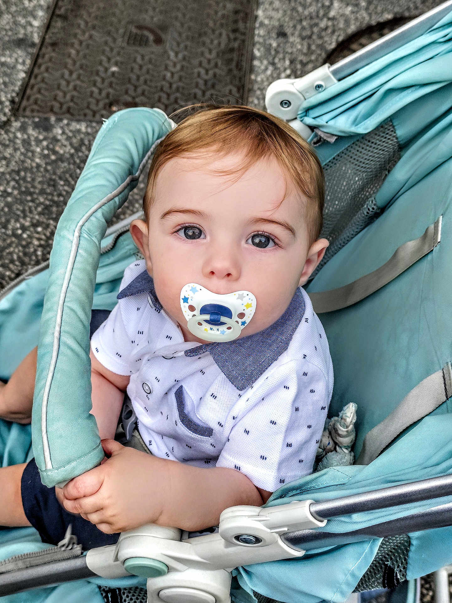 Léandro a rejoint le concours — aidez-le/la à gagner de superbes lots ! baby, pacifier, stroller, child, blue, white_shirt, curious, hand, outdoor, urban, young_child, face, person, infant, seated, clothing, cute, portrait, head, eyes