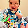 Noah is registered to the contest to win money with this photo: baby, child, smiling, happy, toy, colorful, blanket, plush, foot, hand, curly_hair, clothing, indoors, person, cute, playful, infant, sitting, soft_surface, portrait