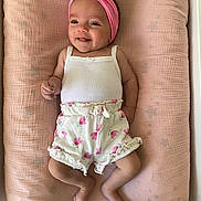 Jena a rejoint le concours — aidez-le/la à gagner de superbes lots ! baby, barefoot, bow, child, clothing, cushion, cute, floral_shorts, happy, headband, indoors, infant, lying_down, person, pink, portrait, resting, smiling, soft_texture, white_top