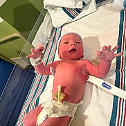Christopher is registered to the contest to win money with this photo: newborn, baby, hospital, bassinet, diaper, medical, wristband, umbilical_clamp, cap, infant, bed, striped_linen, healthcare, patient, child, person, lying_down, nursery, clinic, pink_skin