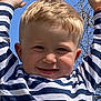 arms_up, blonde_hair, blue_sky, boy, casual_clothing, child, daylight, expression, face, happy, head, nature, outdoor, person, playful, portrait, smiling, striped_shirt, tree_branches, young_child