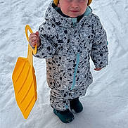 Nino participe au concours pour gagner de l'argent avec cette photo : child, snow, winter_clothing, yellow_shovel, pom_pom_hat, snowsuit, boots, outdoor, cold, snowy_ground, winter_fun, play, young_child, winter_accessories, standing, winter_activity, child_in_snow, hat, gloves, winter_play