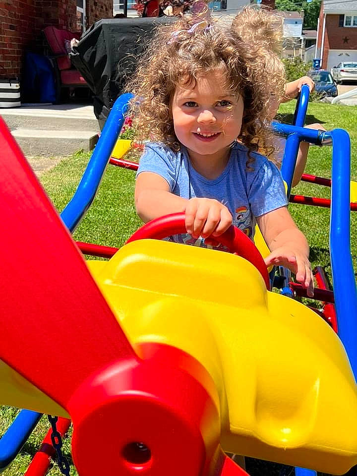 Ruby is registered to the contest to win money with this photo: amusement_park, amusement_ride, child, chute, city, electric_blue, fun, grass, joy, leisure, nonbuilding_structure, outdoor_play_equipment, outdoor_recreation, person, play, playground, recreation, riding_toy, sitting, smile