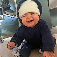 Izaac participe au concours pour gagner de l'argent avec cette photo : baby, child, crawling, smiling, hoodie, hat, pacifier, floor, kitchen, indoor, happy, cute, blue, white, clothing, person, infant, flooring, modern, home