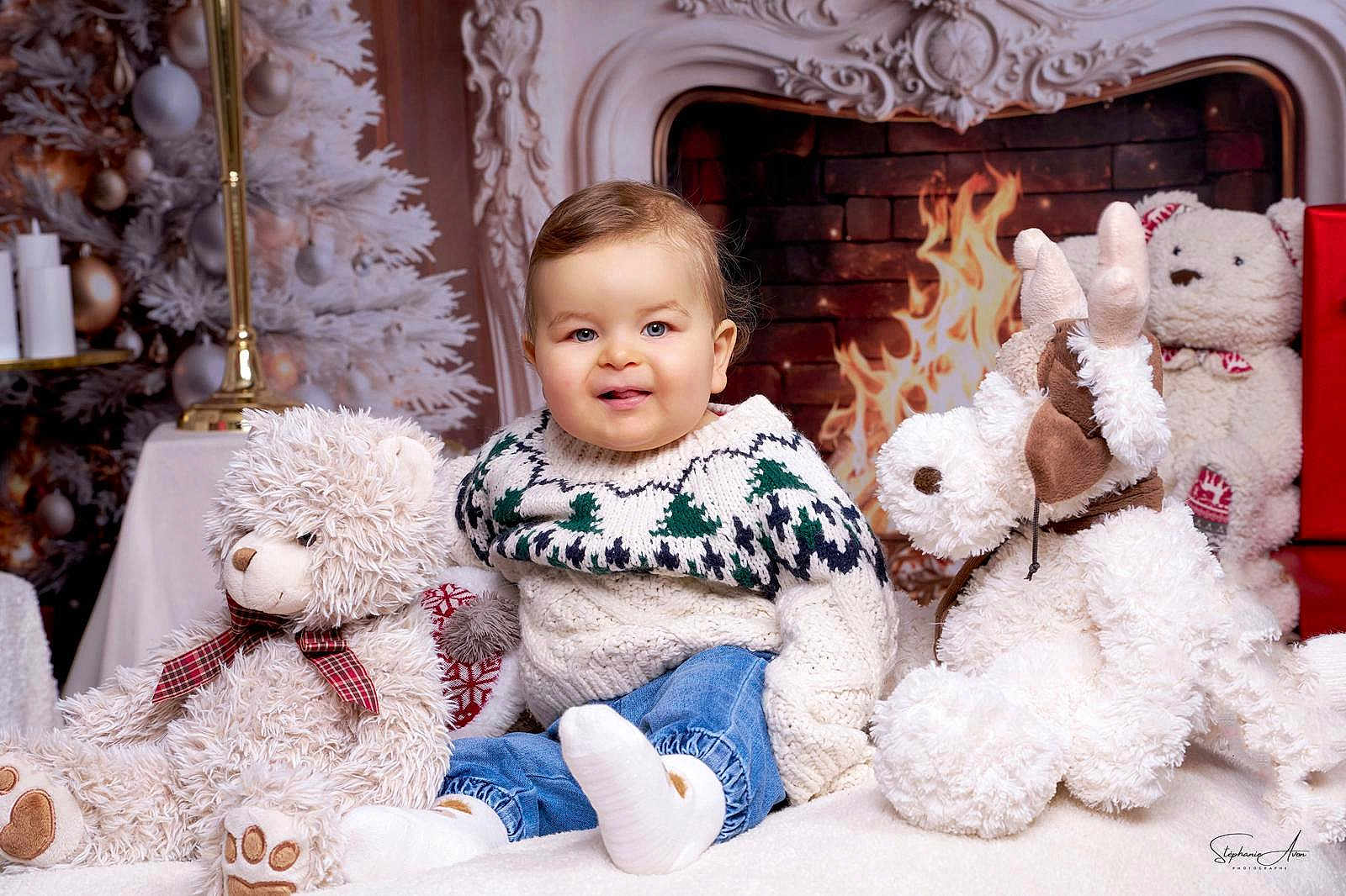 Izaac a rejoint le concours — aidez-le/la à gagner de superbes lots ! baby, child, stuffed_animal, teddy_bear, reindeer, fireplace, christmas_tree, holiday, cozy, sweater, jeans, smiling, indoor, decorations, plush, festive, cute, portrait, winter, warmth