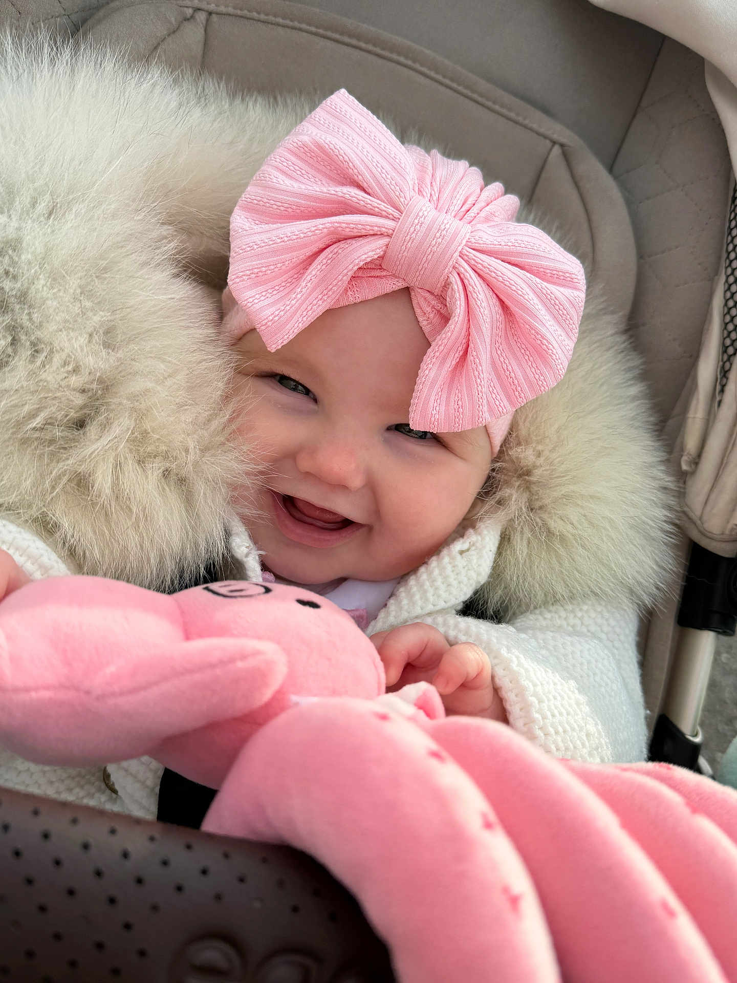 Ophelia is registered to the contest to win money with this photo: baby, child, smile, pink_bow, plush_toy, stroller, coat, fur_trim, happy, cute, infant, clothing, portrait, hand, soft_toy, warm, headwear, closeup, person, baby_accessory